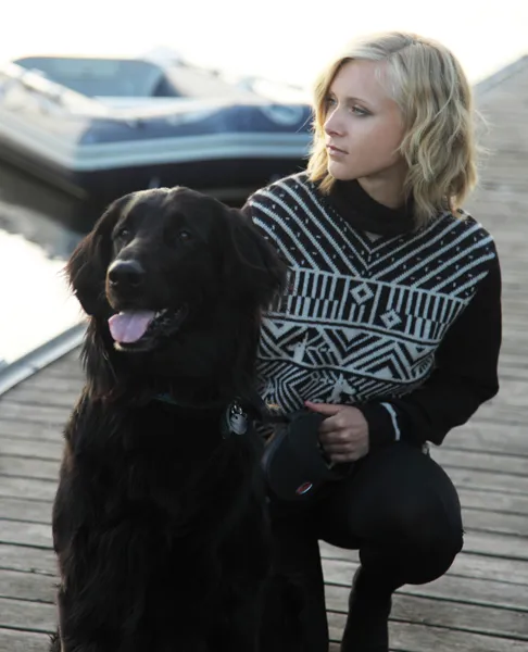 Ung, lyshåret vinne sittende på bryggekanten sammen med sin hund. Ikledd ullgenseren "Fabel" med grafisk mønster