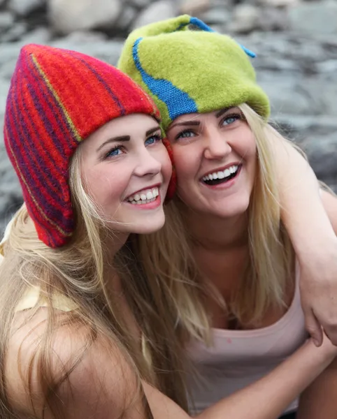 To unge, glade jenter tett sammen ved vannet, ikledd sommertopper og ulluer